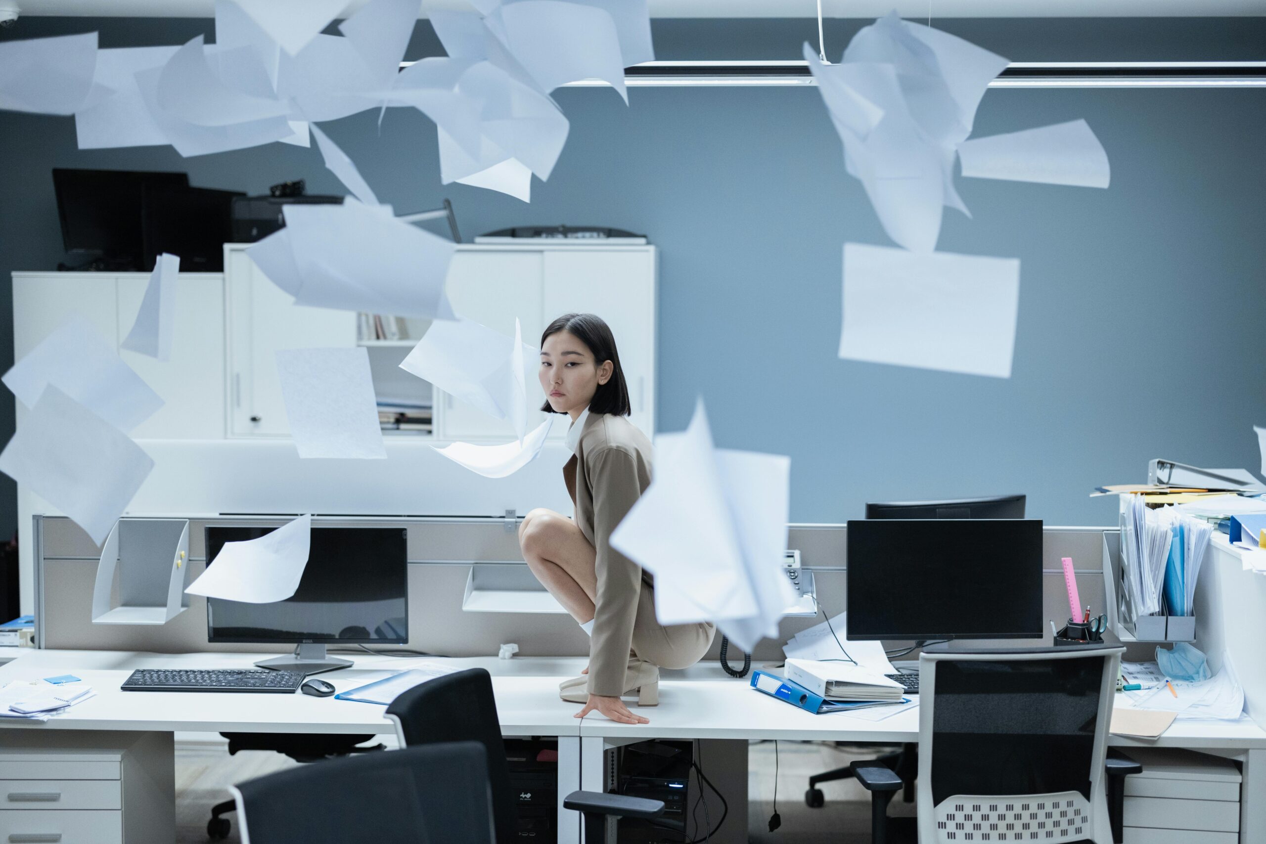 a woman on a table in an office environment, surrounded by paper scattered in the air
