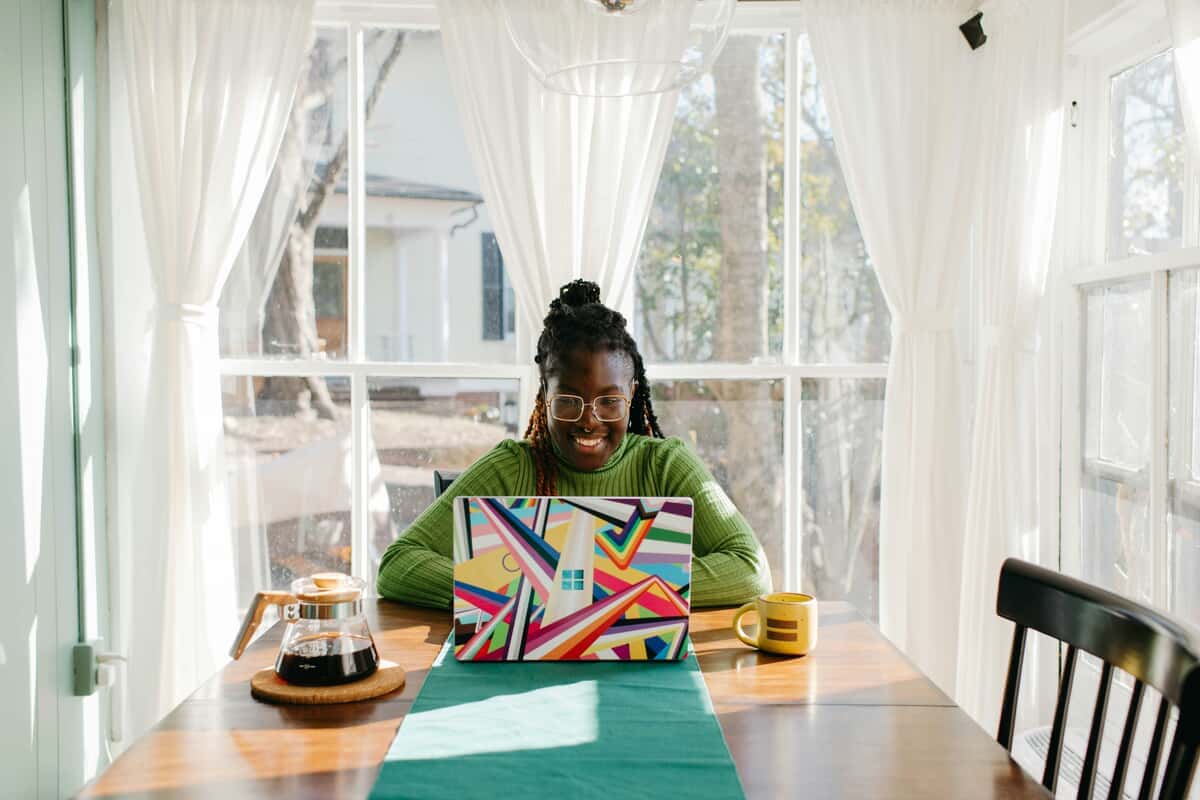 Woman smiling while working on a colorful laptop at home during the day, planning her seasonal side project in a bright workspace.