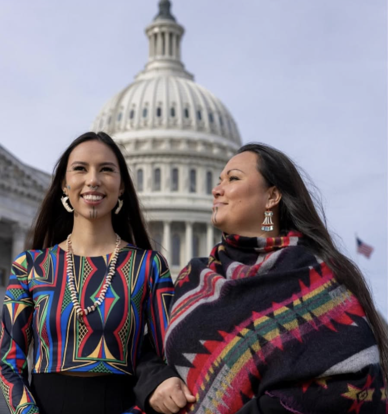 Two Native American women in traditional dress in front of U.S. capitol building.